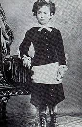 Photographie ancienne de Maria Montessori enfant, debout en robe noire boutonnée